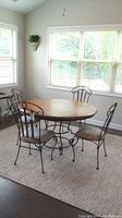 Full dining set in sunroom showing round wooden table with metal base and four metal frame chairs with upholstered seats.