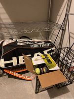 HEAD Tour Team tennis bag with box of Penn tennis balls and wire ball carrier cage on metal shelf