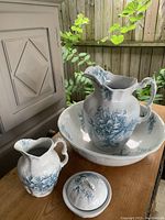Full view of entire 5 piece set: large pitcher, washbowl, small pitcher, lidded container, spoon all decorated with blue floral pattern on white porcelain.