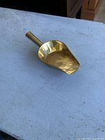 Full view of the polished brass scoop on a white surface showing shape and condition