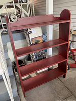 Front view of the antique red wooden shelf with four shelves and shaped top.