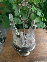 Full view of the Victorian silver-plated cruet set showing the pedestal base, handle, and three glass bottles with one glass stopper; one bottle (oil) missing.