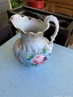 Full view of ceramic water pitcher showing scalloped rim, ornate handle, and floral hand painted decorations.