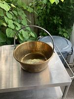 Front and side view of antique brass cooking pot with arched handle, showing overall condition and patina on brass surface.