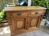 Front view of light wood antique cupboard with two drawers and two doors with raised panel design, showing overall condition and key design elements.