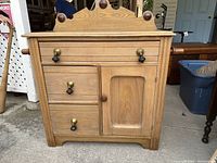 Front view of antique washstand showing three drawers, one door, teardrop pulls, and decorative backsplash with rounded finials.