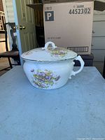 Side/front view of antique ceramic pot with lid showing embossed floral decoration.