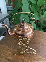 Photo showing a close-up of the copper kettle and its brass handle and spout, highlighting the kettle's detailed curvature and shiny finish.