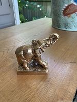 Side view of solid brass elephant paperweight on wooden surface.