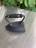 Photo of black cast iron sad iron on silver surface with greenery background.