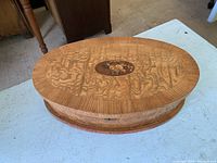 Closed oval wooden box showing detailed floral marquetry design on lid with rich wood grain patterns.