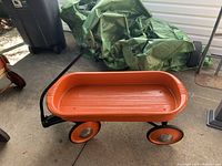 Side view of the orange metal pull wagon showing the handle, body, and wheels