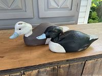 Both solid pine duck decoys placed side-by-side on a wooden surface showing size and relative colors.