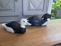 Two wooden duck hunting decoys displayed on a wooden table with a neutral background, showing both decoys side by side.