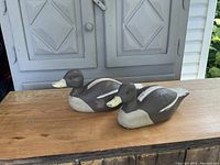 Two vintage wooden duck decoys displayed side by side on a wooden table, showing their overall shape and color.