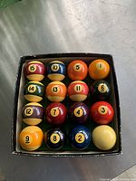 View of 16 pool balls arranged neatly inside original box showing numbering and colors.
