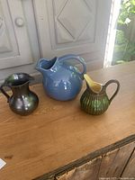 Three vintage pottery pitchers on a wooden surface under natural light.