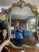 Full view of the large vintage Louis XV style wall mirror held by a person to show scale and condition.