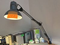 Photo of the gray adjustable metal table lamp on a desk with books and decorative items nearby, showing the lamp extended and angled downward.