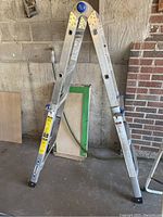 Aluminum folding ladder extended in A-frame shape with blue locking knobs in a garage setting.