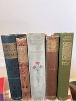 Front view of 5 antique vintage books showing titles and colorful worn spines with decorative details.