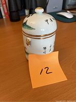 Porcelain jar on wood surface, showing side with black calligraphy and gold accent knob lid.
