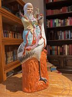 Front view of porcelain sculpture showing elderly man riding crane, detailed traditional robes in bright colors and orange rock base.