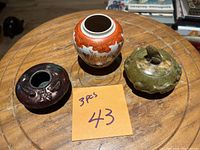Photo showing three antique decorative items: a porcelain vase with orange floral pattern, a round jade lidded container with carved frog finial, and a dark glazed vessel with ornamental motifs.