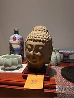 Frontal view of marble Buddha head on wooden base showing facial details and overall form