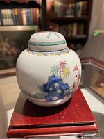 Side angle of porcelain jar showing painted Asian figures, plants, and decorative motifs.