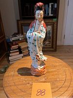 Front view of the porcelain Guan Yin sculpture on a wooden table with some books and framed art in the background.