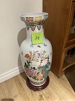 Front view of the tall porcelain vase with floral and bird designs and a wooden base.