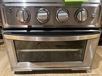 Front view of stainless steel mini electric oven showing control panel with knobs and glass door.