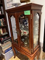 Side angle view of the mahogany display cabinet showing its glass door panels and visible shelving inside.