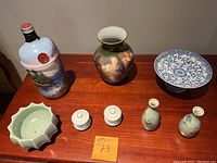 Overview of lot showing painted glass bottle, large porcelain vase, blue and white pedestal bowl, pale green bowl, lidded porcelain cups, and two small porcelain vases.