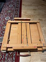 Folded small wooden easel with paint marks lying flat on the floor.