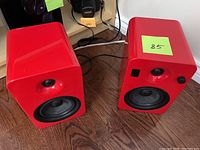 Two red Kanto Yumi speaker units on wood floor with power and audio cables visible behind them.