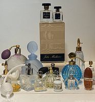 Overview photo showing a variety of vintage perfume bottles including Pierre Balmain Jolie Madame bottles and other miniature and decorative bottles with atomizers and spray nozzles in various shapes and colors.