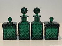 Front view of four green diamond cut crystal perfume bottles, two tall with faceted stoppers and two square with lids and smaller stoppers