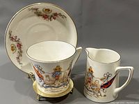 Photo showing full set of the 1911 King George V coronation cream, tea cup and saucer with detailed royal and floral designs.