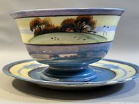 Close-up view of the berry bowl resting on the hand-painted saucer showing intricate landscape hand-painted design with house, trees, and water reflection.