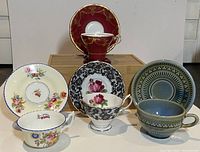 Photo of five different porcelain teacups and saucers arranged in a group showing various floral and decorative styles.
