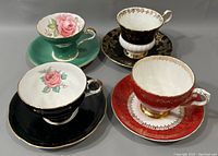 Four teacup and saucer sets displayed with cups upright showing interior floral designs and gold trim on handles and rims.