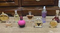 All 9 perfume bottles arranged on a wood surface, showing size and shape differences, including recognizable brand bottles.