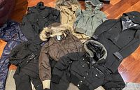 Group photo of seven fall/winter jackets including various styles like puffers and hooded jackets laid out on floor