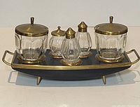Front view of complete condiment set on black tray with brass edges and legs.