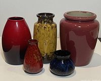 Five Mid-Century Modern pottery vases arranged in a row showing different shapes, colors, and sizes including two yellow and red glazed pieces, a burgundy vase, and smaller blue and red pieces.