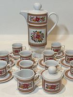 Photo showing the entire set with lidded coffee pot, sugar bowl, creamer, and espresso cups on saucers, all decorated with floral and stripe patterns.