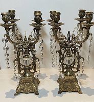 Pair of antique 4-arm brass or bronze candelabra with claw feet and hanging crystal prisms on white background, front view