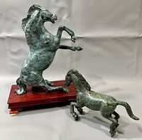 Pair of patinated bronze horse figurines displayed on grey background, showing overall view including wooden base.